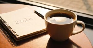A cup of coffee beside a notebook labeled 2026 in warm morning light - Warm, welcoming image symbolizing a personal growth journey and life realignment