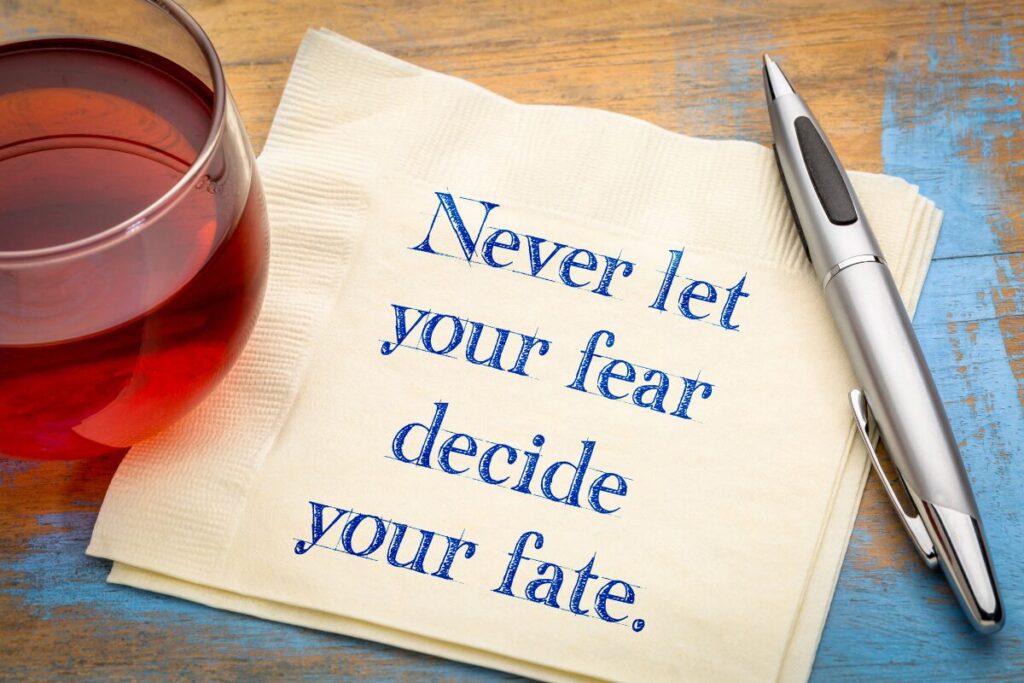 A folded napkin on a wooden table with a glass of tea and a pen beside it, featuring the printed message: “Never let your fear decide your fate.