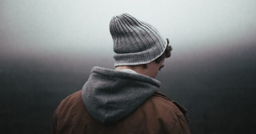 Person wearing a jacket and hat standing in fog, looking down quietly
