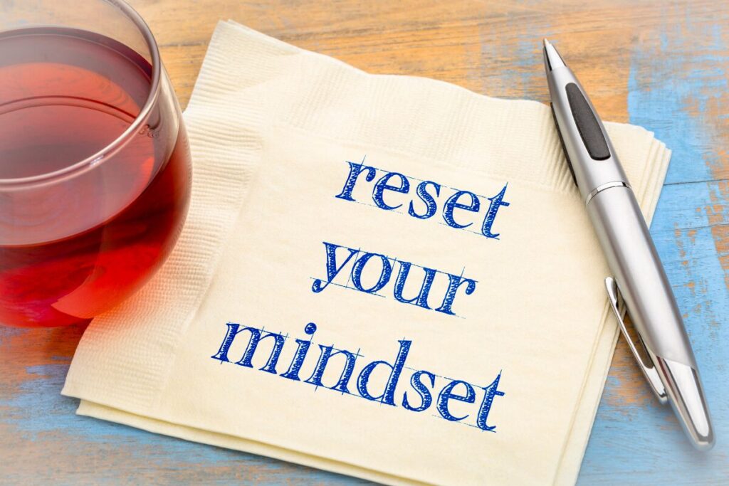 Handwritten note reading “reset your mindset” next to a cup of tea on a wooden surface