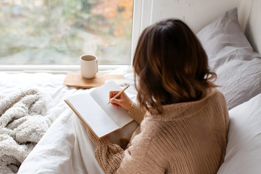 Person sitting on a bed with a notebook and coffee, pausing to reflect and learn how to stop overthinking