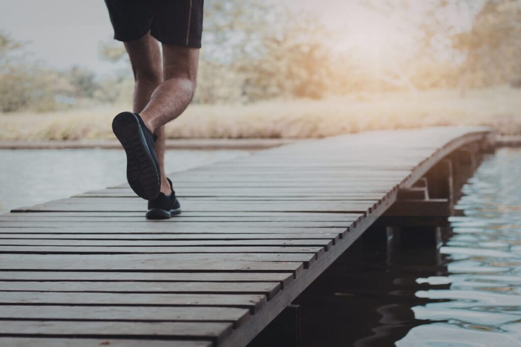 Person walking forward on a wooden boardwalk near water on a sunny day
