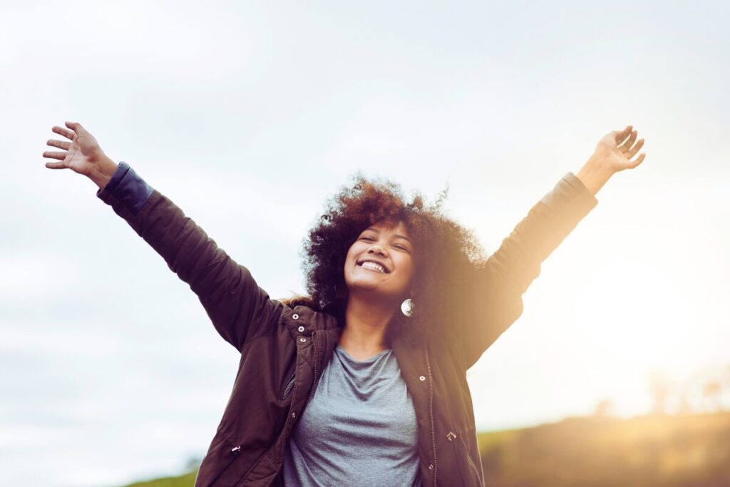 Person standing outdoors with arms raised, smiling confidently, representing a fresh start and personal growth in the new year. Building momentum that lasts through consistent personal growth