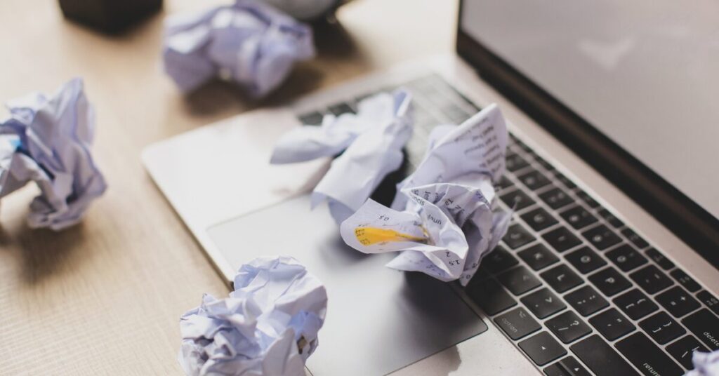 Laptop keyboard covered with crumpled sheets of paper during a writing session, representing how to stop being a perfectionist and embrace imperfect progress.