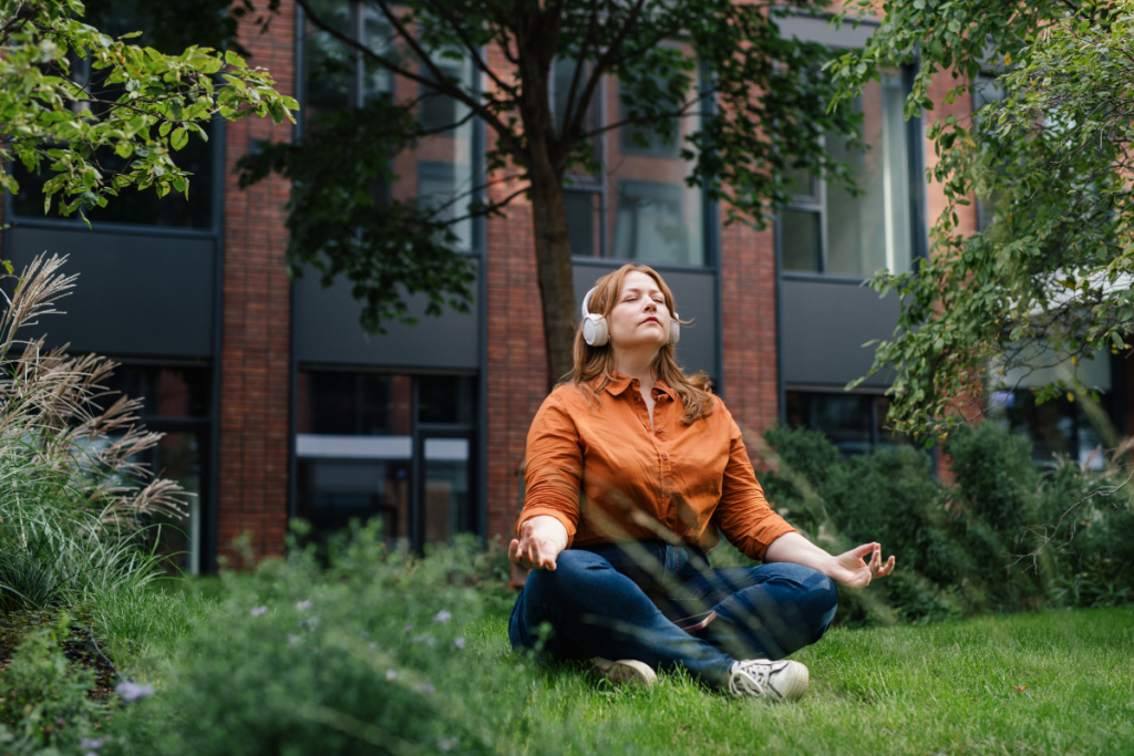 ull-figured woman with headphones meditating cross-legged on grass in a city garden