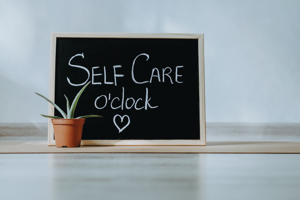 halkboard sign reading "Self Care o'clock" with a small potted succulent on a wooden shelf