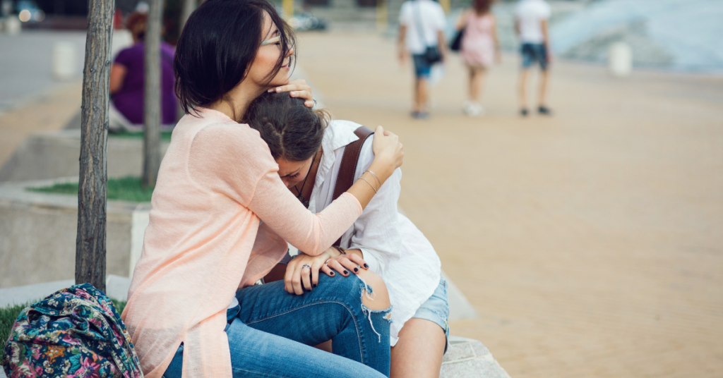 Woman comforting another woman sitting outside showing emotional support
